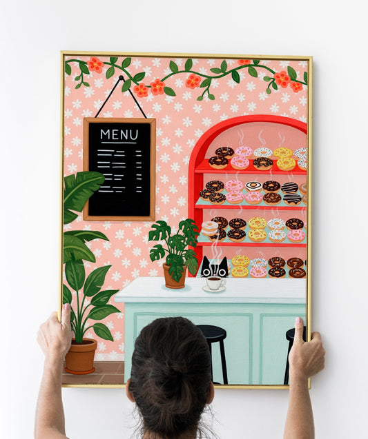 A whimsical illustration of a cozy donut shop featuring a black cat with wide eyes peeking over a coffee counter. Behind the cat is a red shelf filled with steaming colorful donuts in various flavors and toppings. A cup of coffee, potted plants, a menu board, and a pink floral wallpaper complete the cozy café scene. The artwork is playful and vibrant, ideal for bakery or kitchen wall decor, especially for cat and pastry lovers.