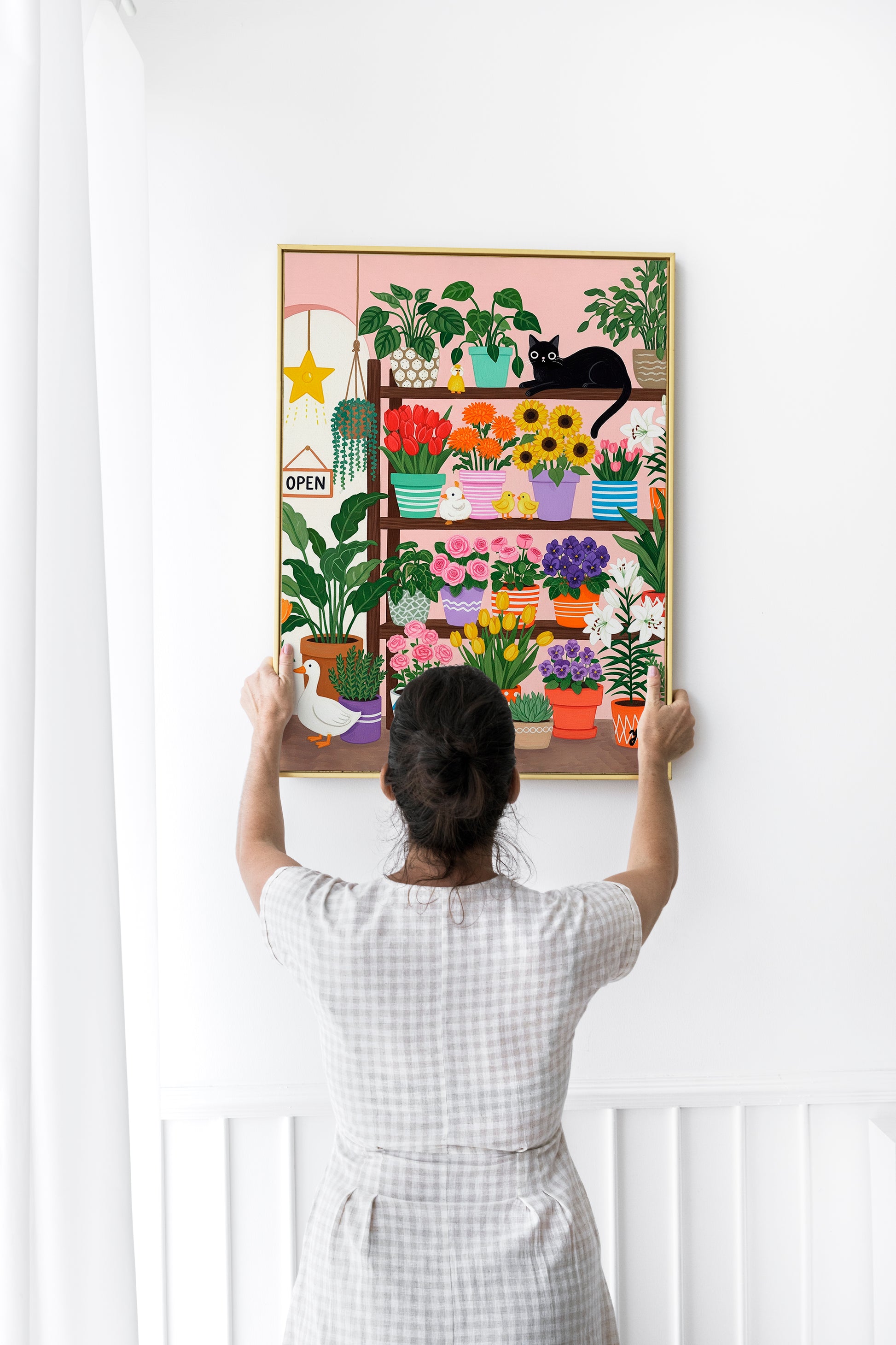 A whimsical illustration of a cozy flower shop filled with colorful potted flowers like tulips, roses, sunflowers, and lilies. A black cat lounges on a shelf, surrounded by cheerful ducks and a white goose. The scene is bright, playful, and perfect for spring or cottagecore decor.
