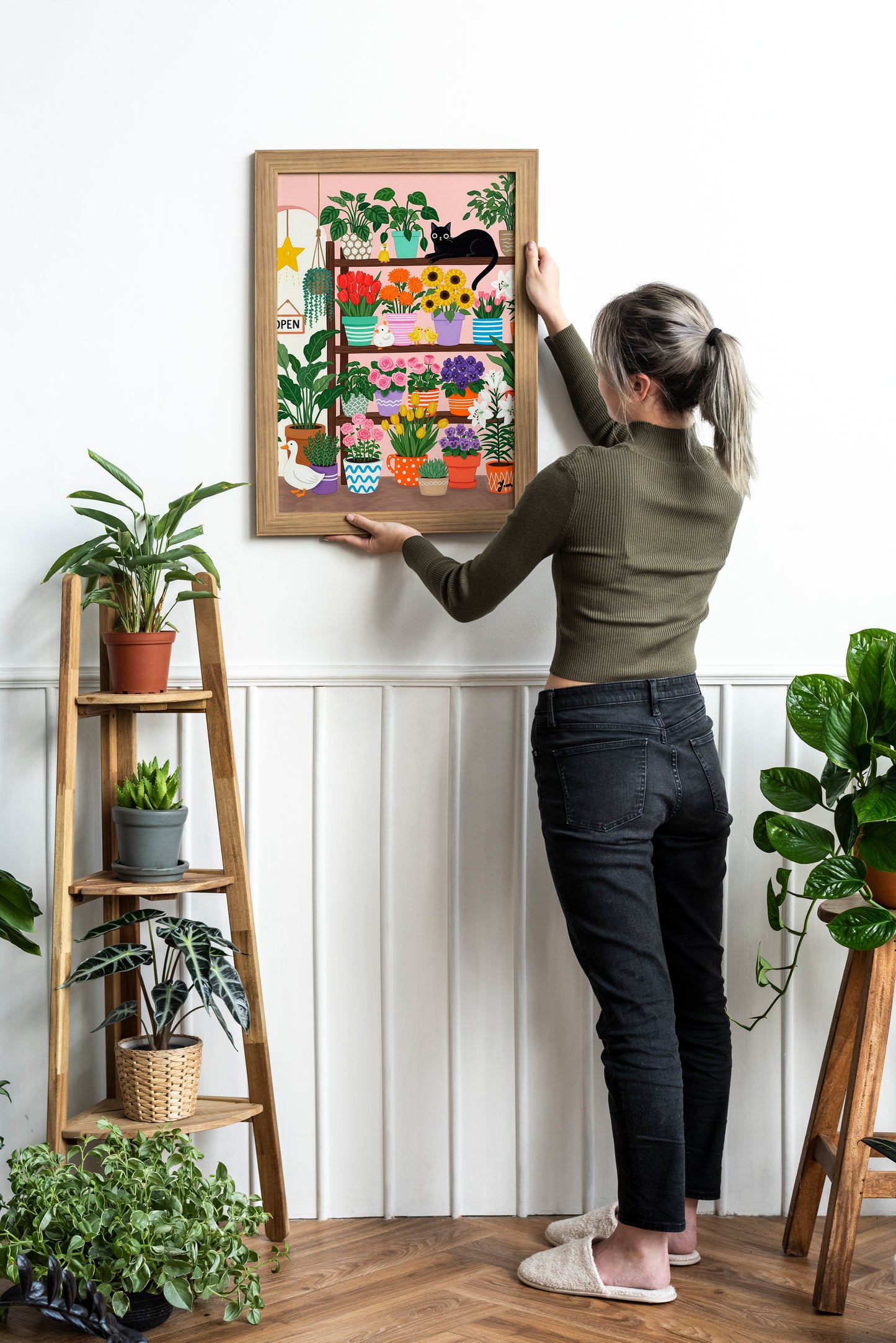 A whimsical illustration of a cozy flower shop filled with colorful potted flowers like tulips, roses, sunflowers, and lilies. A black cat lounges on a shelf, surrounded by cheerful ducks and a white goose. The scene is bright, playful, and perfect for spring or cottagecore decor.
